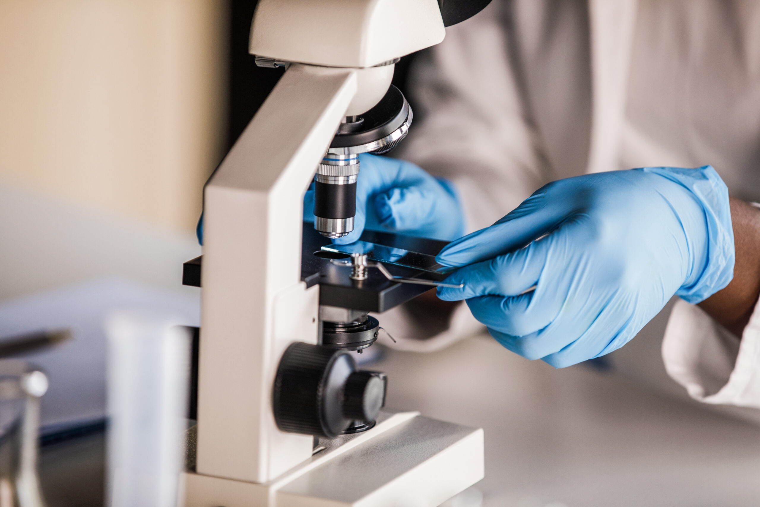 Forensic lab technician in gloves placing a DNA sample slide under a microscope
